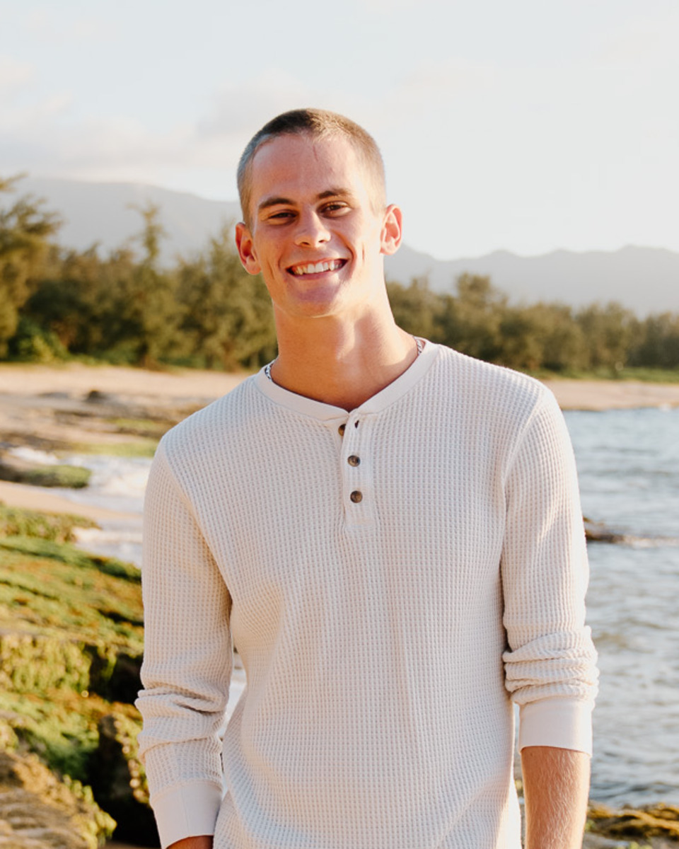 Anthony on the beach at golden hour, in a cream henley, smiling.
