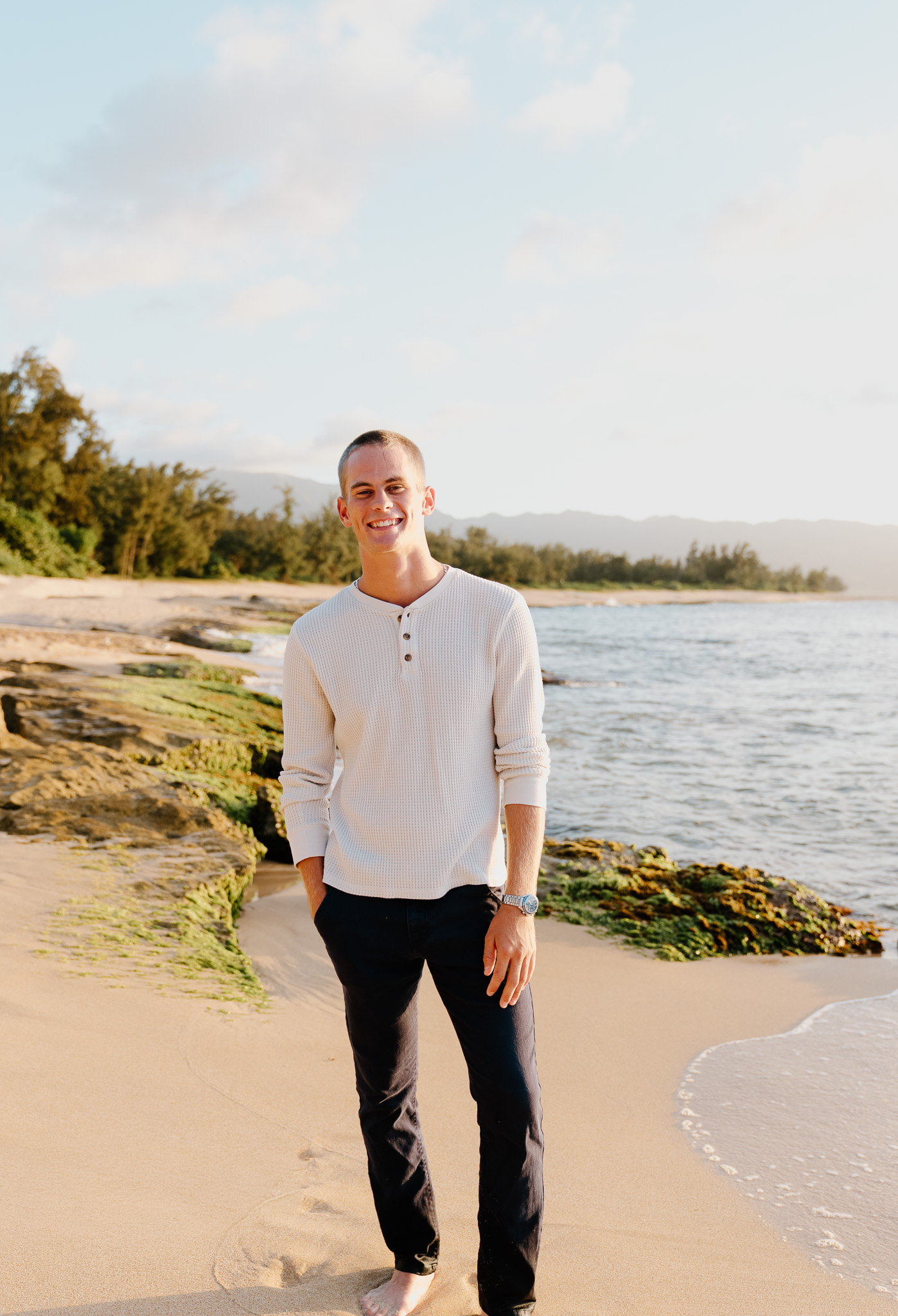 Anthony on the beach at golden hour, in a cream henley, smiling.